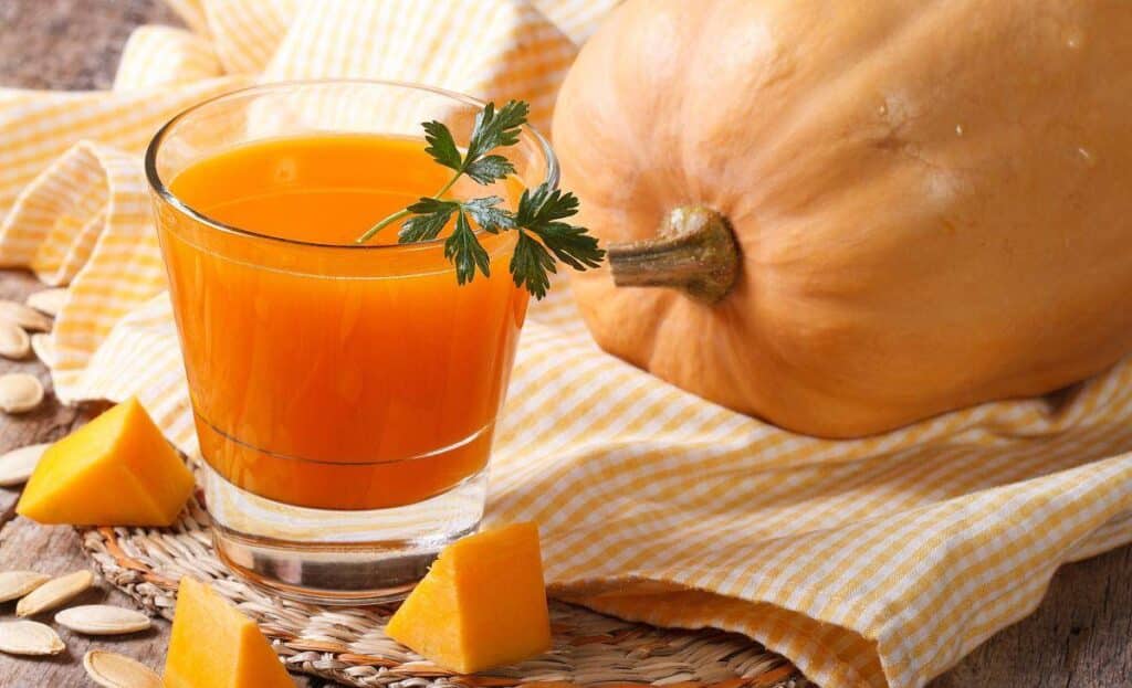 단호박 주스가 담긴 유리컵과 통호박이 함께 놓인 장면으로, 단호박의 영양을 간편하게 섭취할 수 있는 형태를 상징함 A glass of sweet pumpkin juice beside a whole pumpkin, symbolizing easy nutrient intake from pumpkins