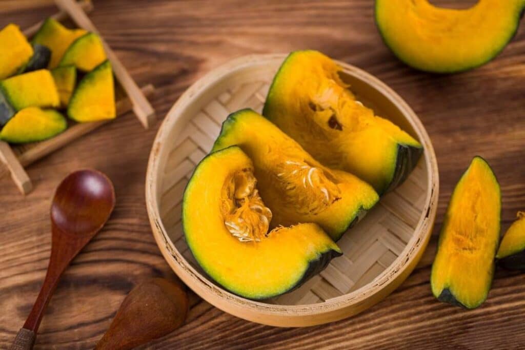 잘 익은 단호박 조각이 대나무 찜기에 담긴 모습으로, 단호박의 풍부한 베타카로틴과 건강한 식단 이미지를 표현한 장면 Steamed slices of sweet pumpkin in a bamboo tray symbolizing rich beta-carotene and a healthy diet