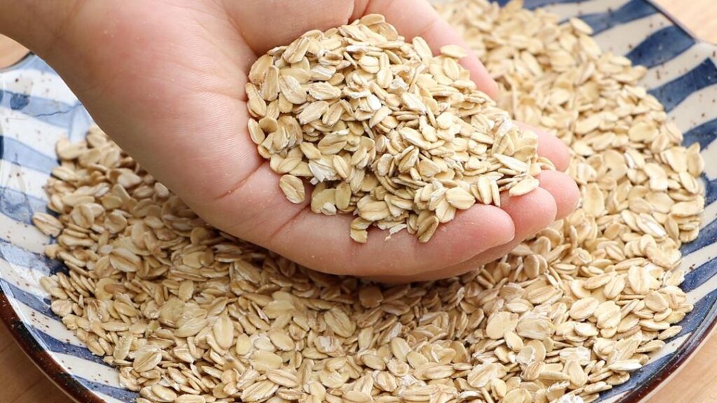 손에 귀리 플레이크를 담고 있는 모습으로, 건강한 식습관과 곡물의 영양 가치를 상징하는 이미지 A hand holding rolled oats, symbolizing healthy eating and the nutritional benefits of grains