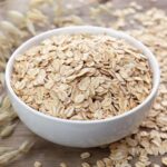 하얀 그릇에 담긴 귀리 플레이크로, 풍부한 식이섬유와 단백질이 함유된 건강 곡물을 보여주는 이미지 A white bowl filled with rolled oats, showcasing a healthy grain rich in fiber and protein