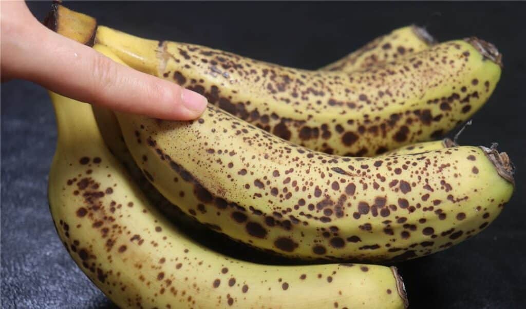 갈색 반점이 생긴 잘 익은 바나나를 손가락으로 누르는 장면으로, 항산화 성분이 증가한 바나나의 특징을 보여주는 이미지 A hand pressing ripe bananas with brown spots, showing the increased antioxidants in overripe fruit