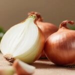 갈색 껍질의 양파와 반으로 자른 양파가 함께 놓인 모습으로, 항산화 성분이 풍부한 양파의 신선함을 보여주는 이미지 Fresh brown-skin onions, one cut in half, illustrating the freshness and antioxidant richness of onions